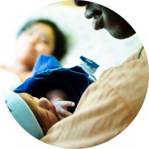 Imagem do pai segurando o bebê recém nascido no colo e a mãe na cama observando